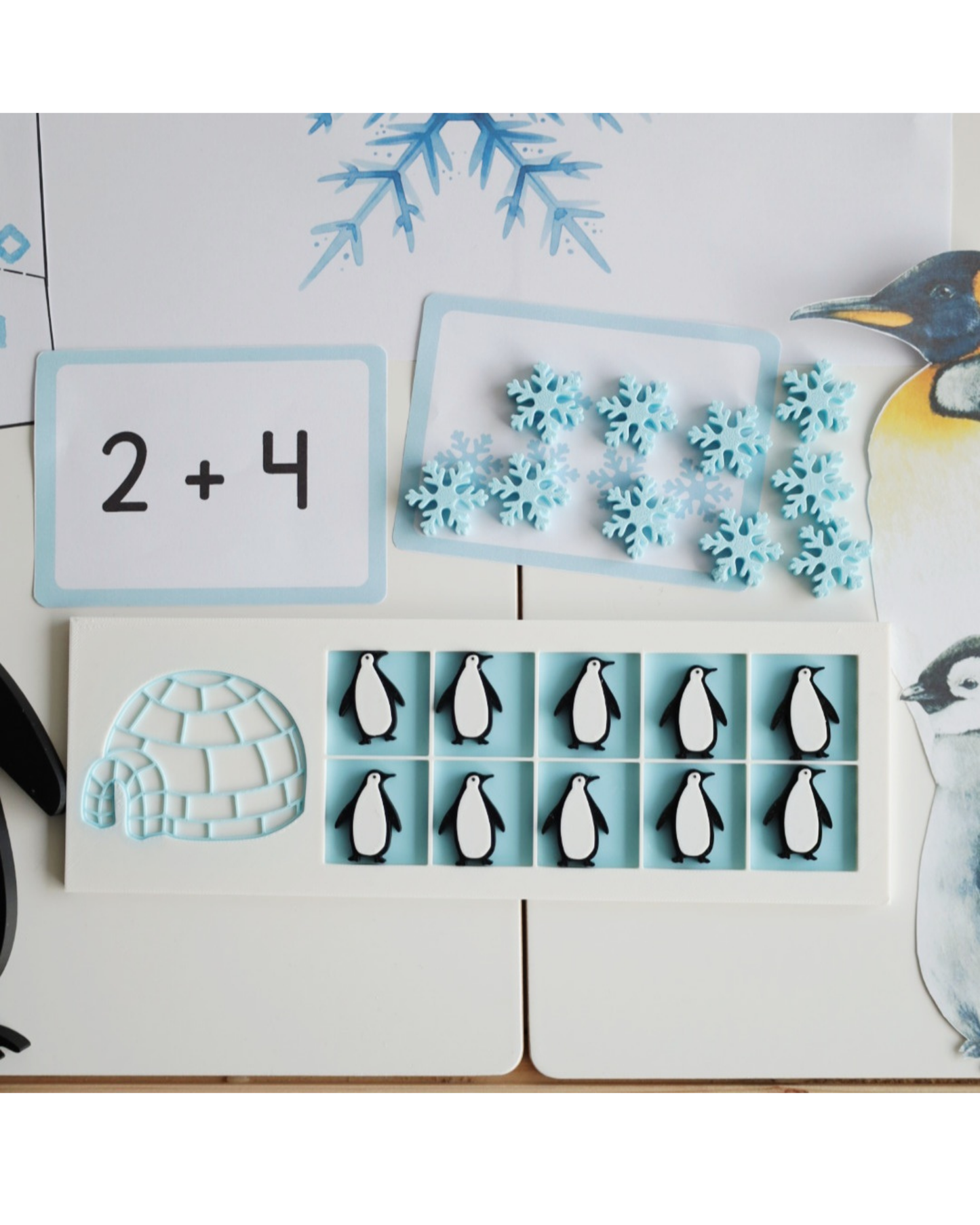 Tabliczka do liczenia 10 Frame Igloo Playtessori z liczmanami pingwinami i sniezynek, pokazana wraz z zimowymi kartami matematycznymi i ilustracjami do pracy sensorycznej.