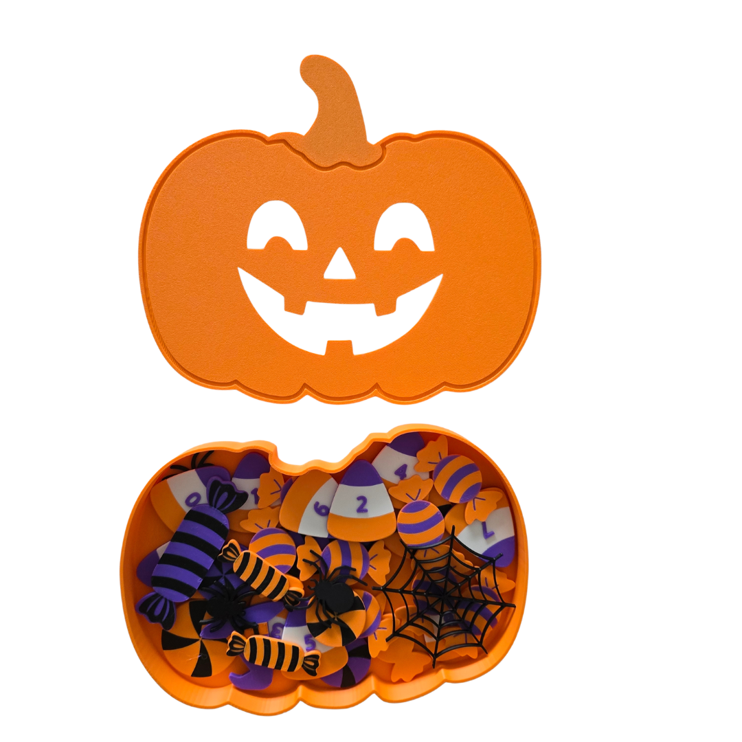 An orange pumpkin-shaped Halloween candy box with a carved jack-o'-lantern lid and an open bottom section filled with purple, orange, and black candy pieces, shown on a white background.