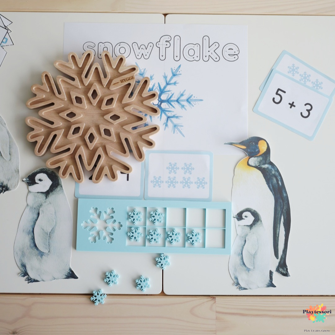 Drewniana wysypywanka sensoryczna śnieżynka w zimowej aranżacji z kartami matematycznymi i pingwinami, zimowa aktywność Montessori.