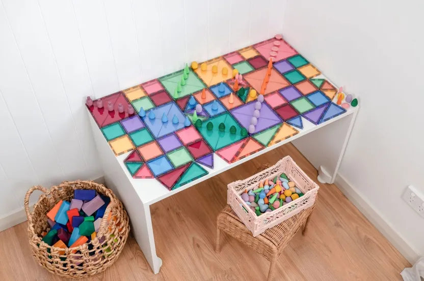 Children's play table with colorful geometric tiles and toys on a wooden floor.