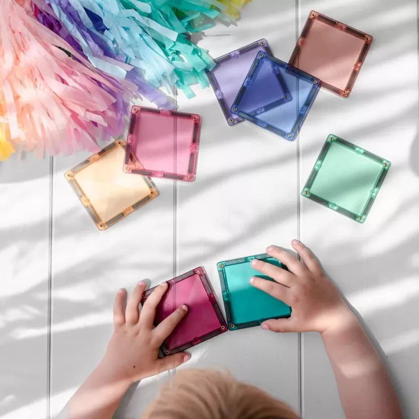 Colorful transparent square blocks on a white surface with children's hands interacting with them.