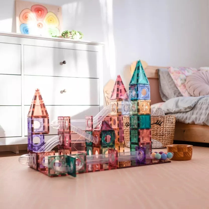 Colorful magnetic building blocks on a wooden floor with a bed and dresser in the background.