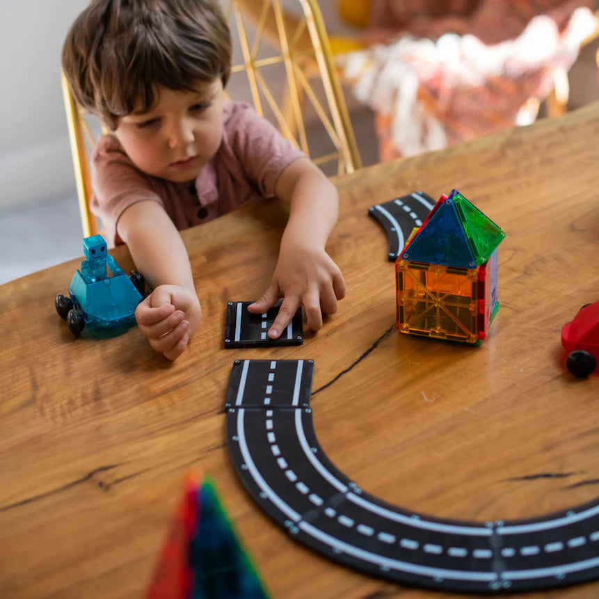 Child playing with toy cars and tracks on a wooden table