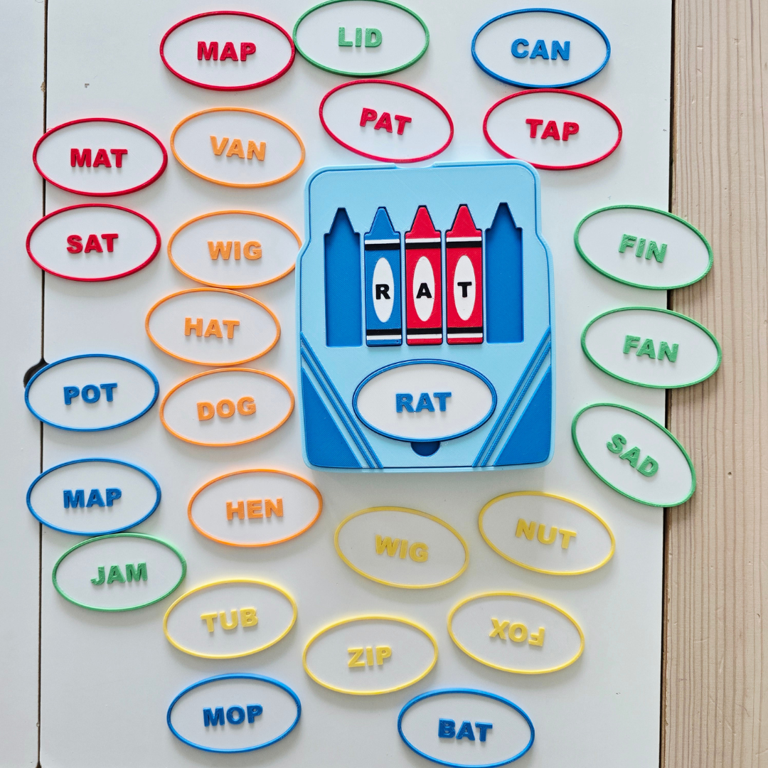 Close-up of crayon box tray with letter tiles spelling RAT, matched to a blue oval label, CVC word building activity