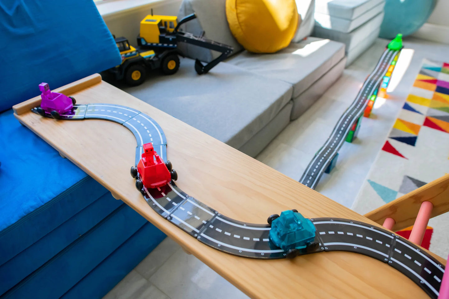 Toy train set on a wooden table with colorful tracks and cars in a room setting.