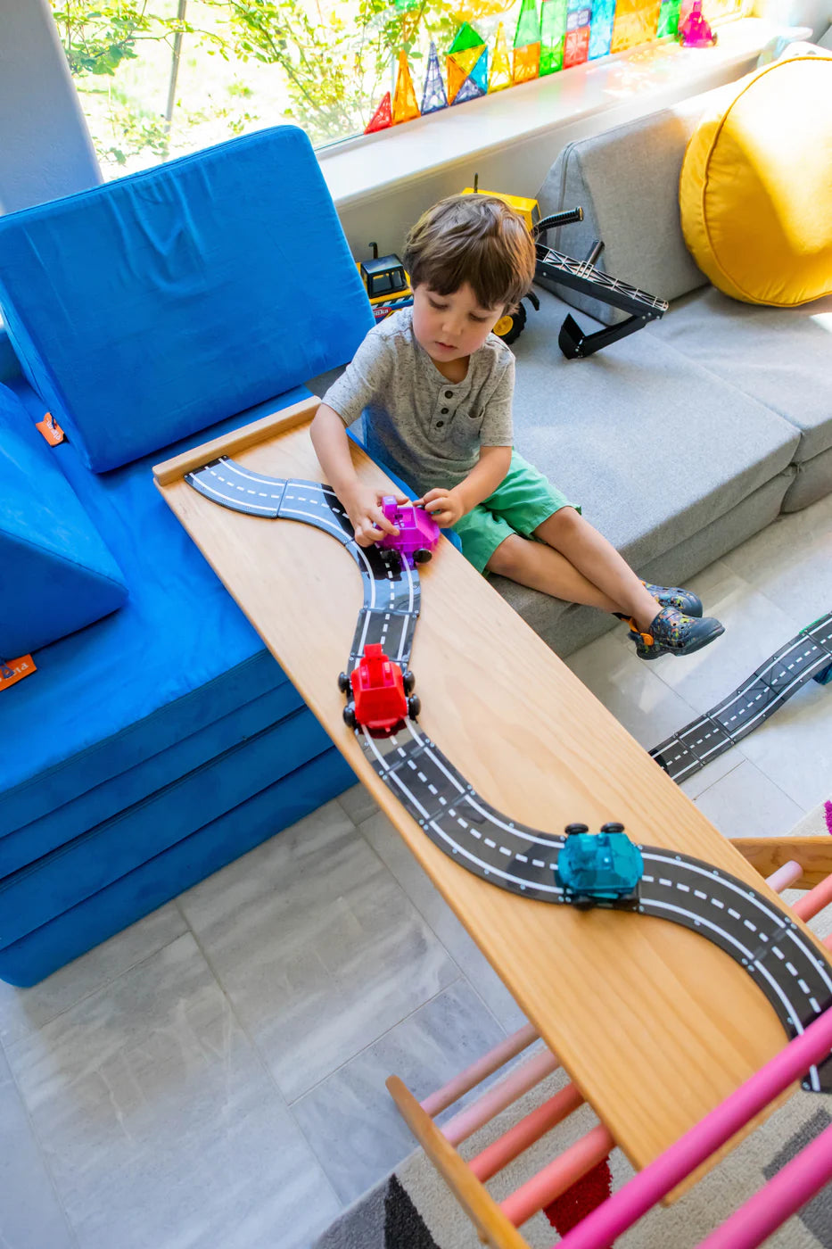 Child playing with a toy train set on a wooden table in a living room.