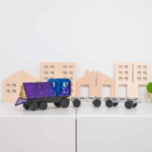 Toy dump truck with a blue container on a white surface with wooden house models in the background