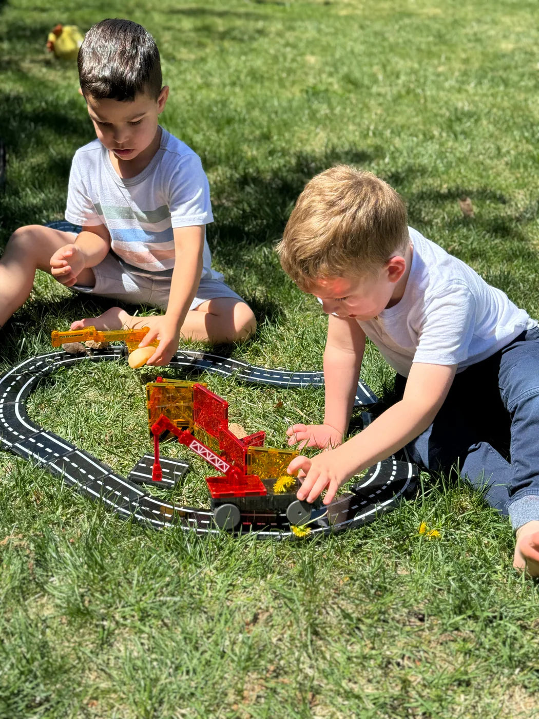 Two children playing with a toy train set on grass