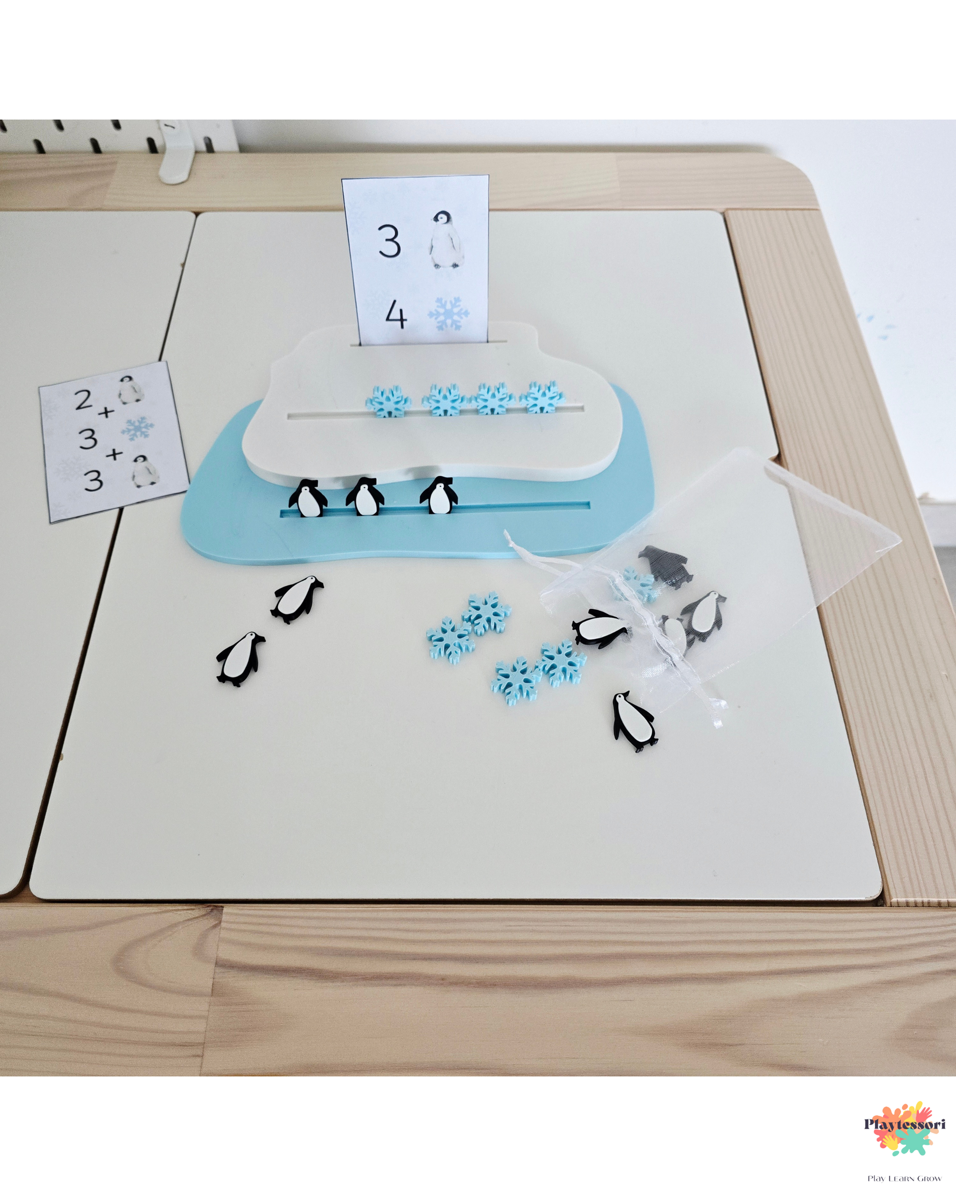 Edukacyjna taca lodowa z pingwinami i śnieżynkami do liczenia; widoczne są także karty z działaniami matematycznymi i woreczek z dodatkowymi liczmanami.