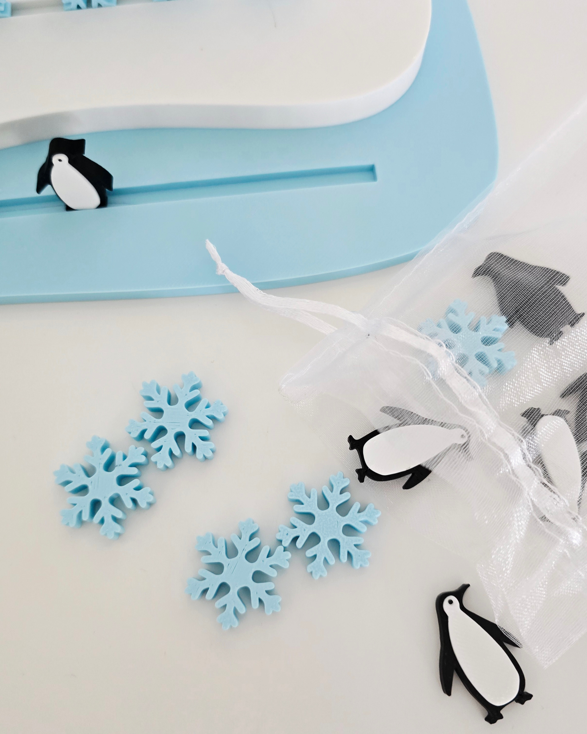Zbliżenie na niebieskie liczmany w kształcie śnieżynek i czarno-białe pingwiny, wysypane obok woreczka z zestawu do liczenia Arktyka