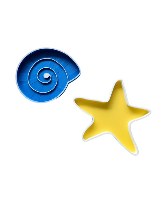 Yellow starfish sensory tray and blue spiral shell sensory tray placed on kinetic sand on a round white Montessori tray — Playtessori ocean beach small world sensory play set for toddlers