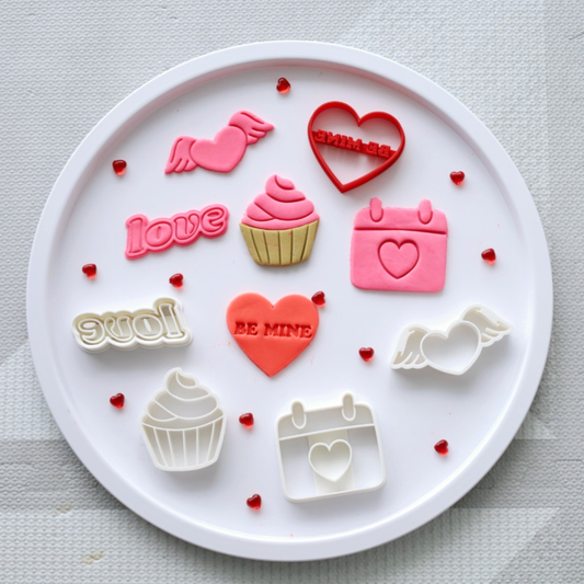 Round tray with Valentine’s Day play dough cutters in shapes like hearts, cupcakes, wings, and the word "love", surrounded by small red heart gems.