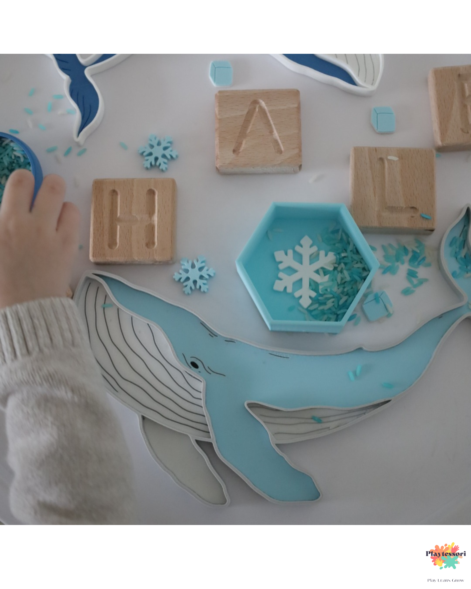 Humpback whale sensory play tray setup with blue sensory rice, wooden letter blocks spelling WHALE, snowflake counters and hexagon bowl on a round white Montessori tray — Playtessori ocean collection